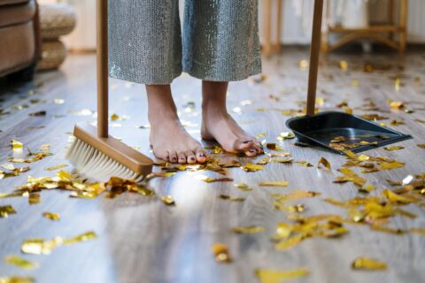 A professional cleaner from Mindful Cleaning Services stands amidst confetti, holding a dusty bin and duster, ready to clean up after a special event.