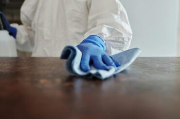 A professional cleaner from Mindful Cleaning Services wearing gloves and holding eco-friendly cleaning supplies in a Boonton, NJ kitchen.